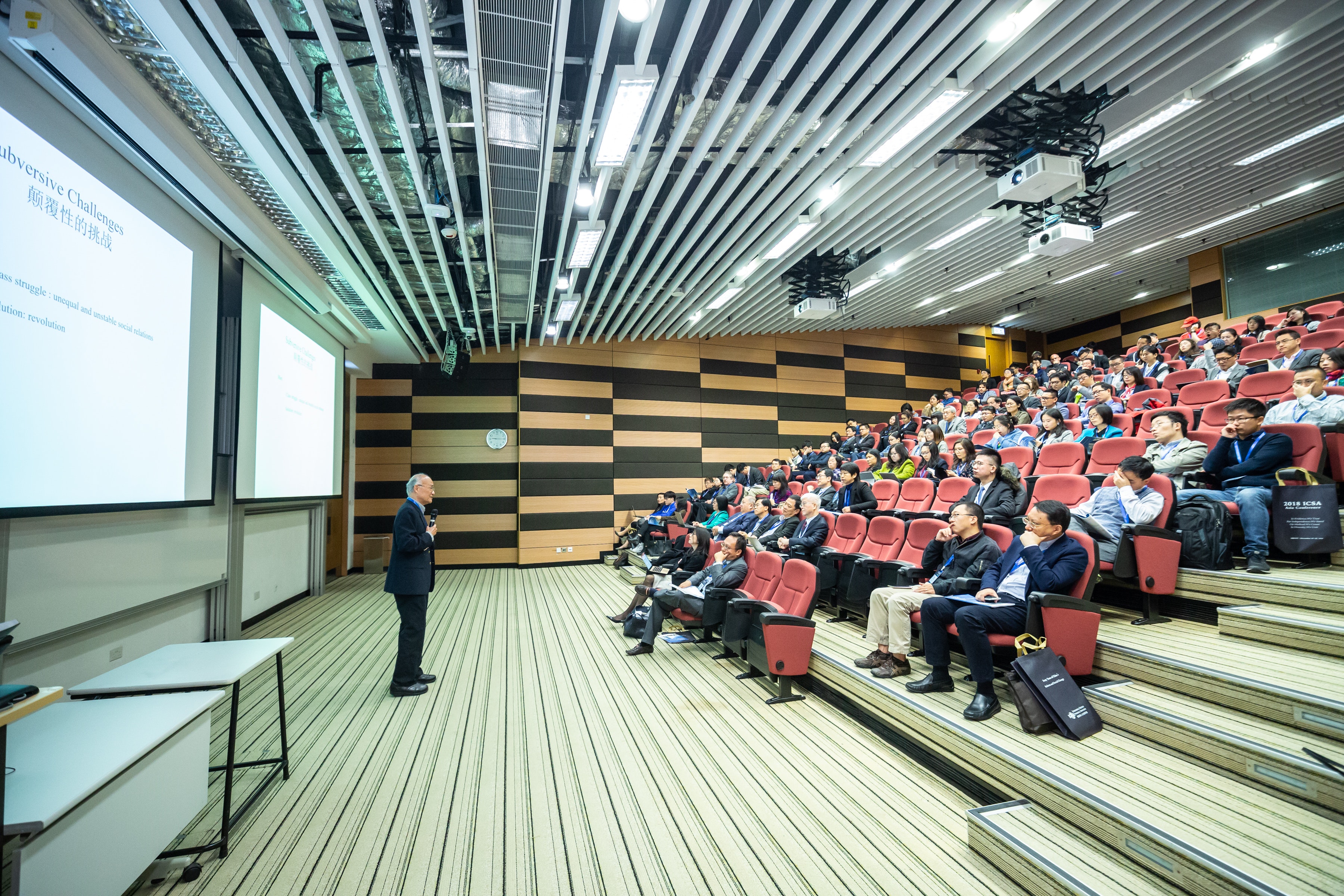 Elderly white male speaker presenting in front of an auditorium hall