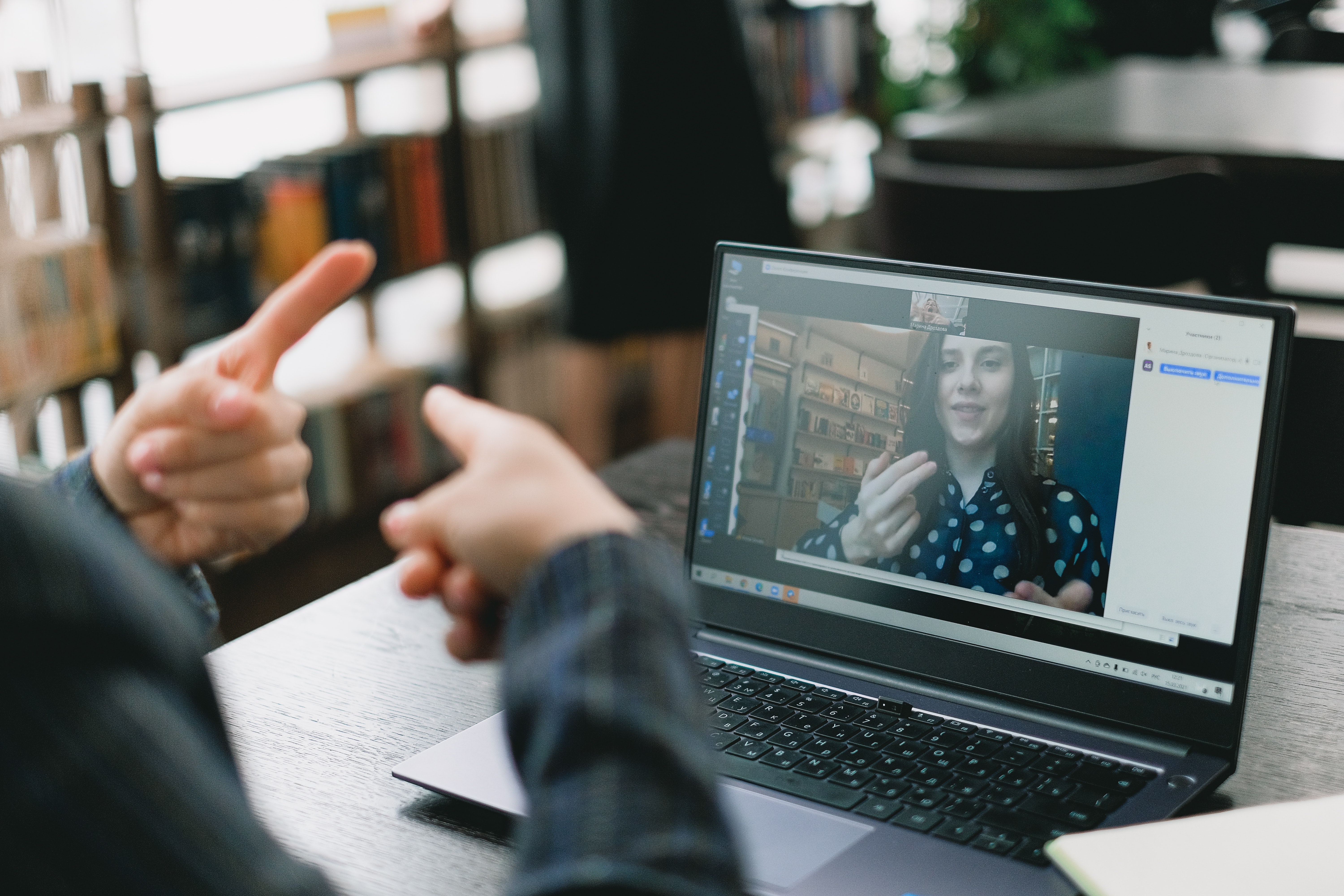 White woman in her 20’s, wearing polka dots and is learning sign language during online lesson with white, female tutor